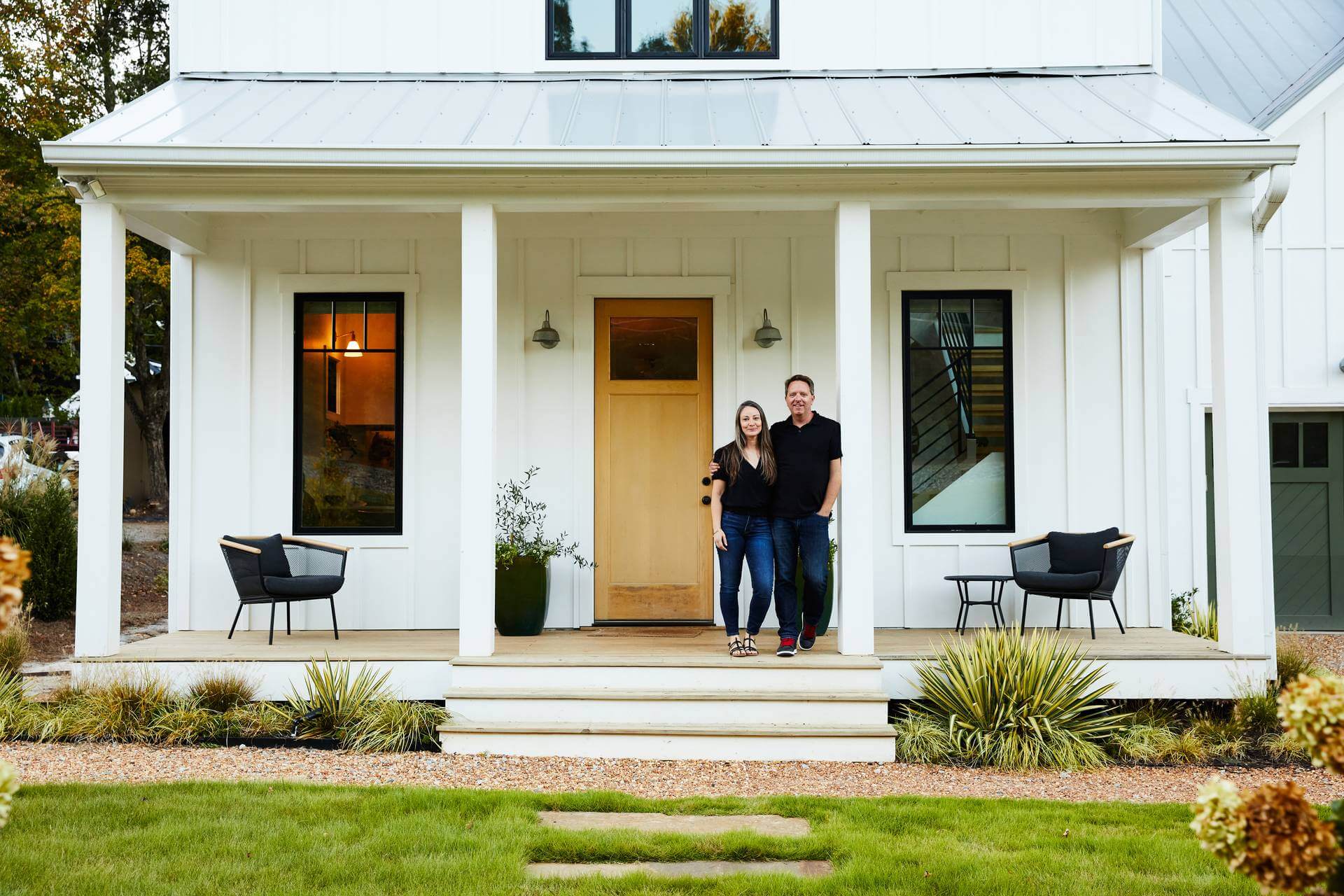 Man and woman stand together on the front porch of their modern farmhouse