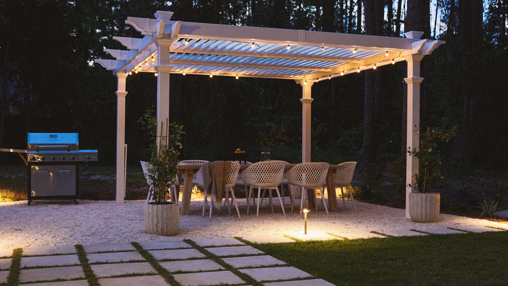 Backyard at night with pergola-covered dining area with string lights
