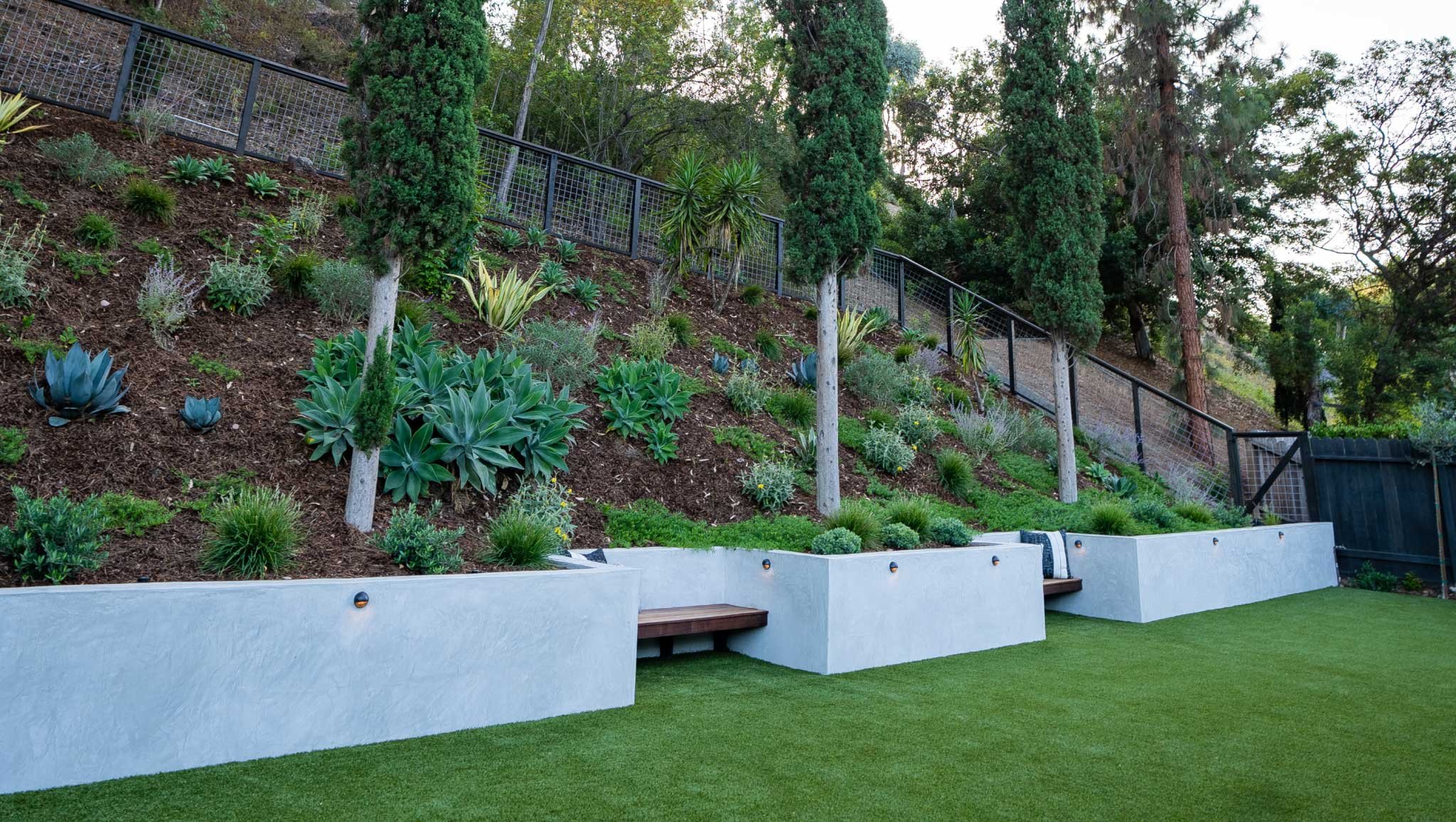 Sloped section of yard with modern retaining wall with built in benches and plantings all over slope