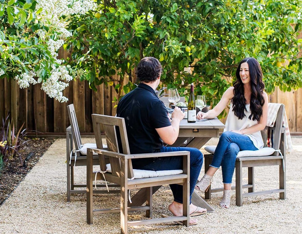Steve and Kacey sitting at an outdoor dining table on a gravel patio surrounded by planting beds