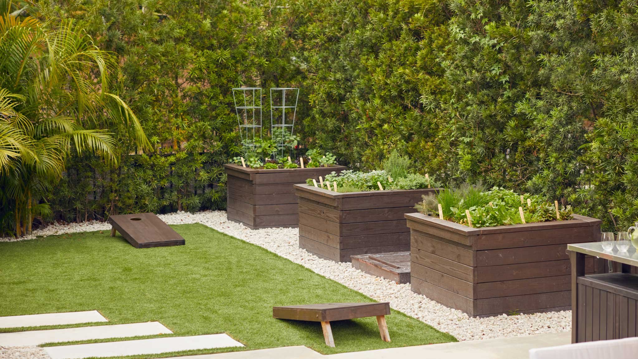 backyard corner with cornhole on lawn and raised bed garden