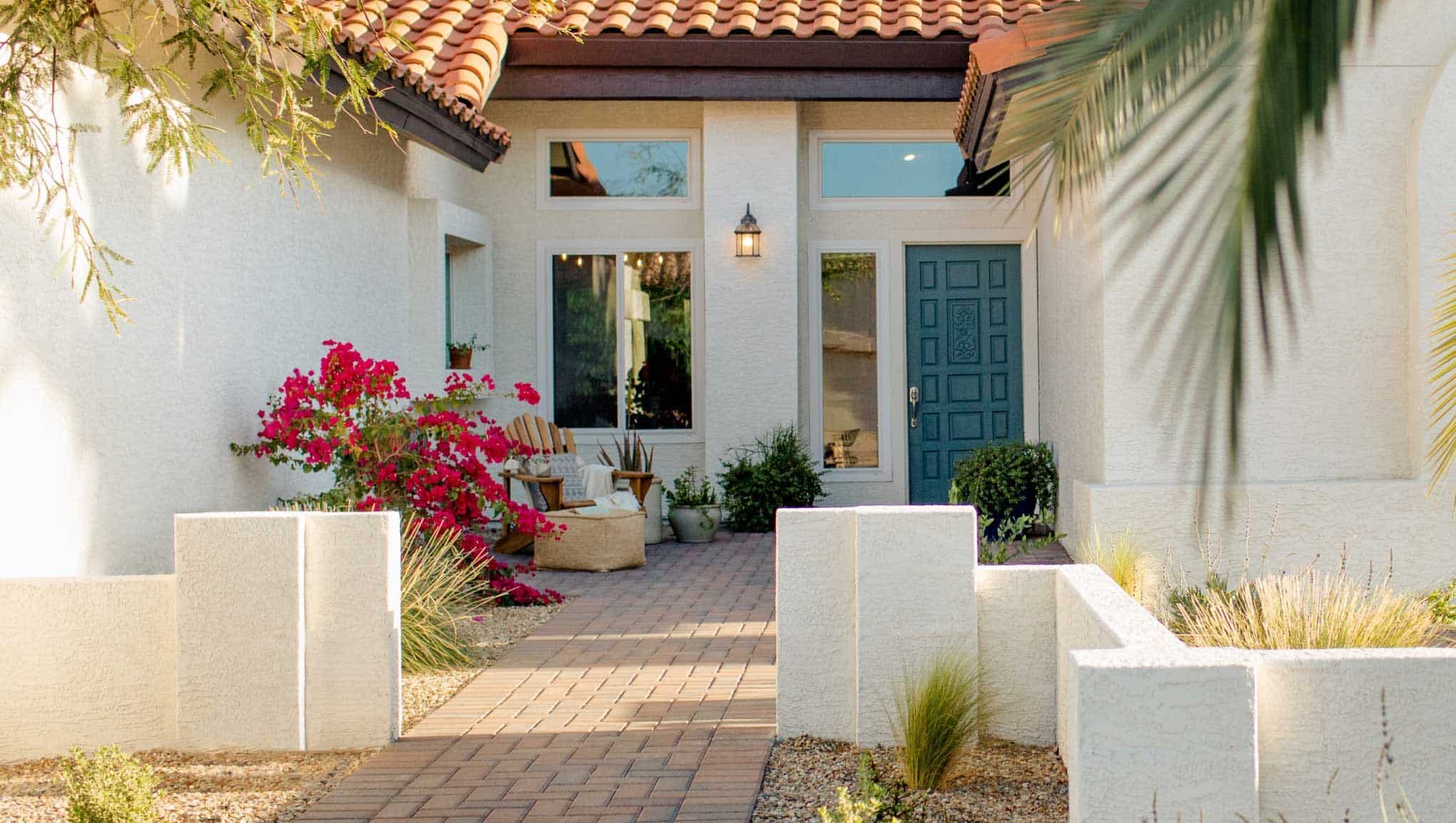 Close up of home entryway with brick walkway, blue front door, and colorful plantings