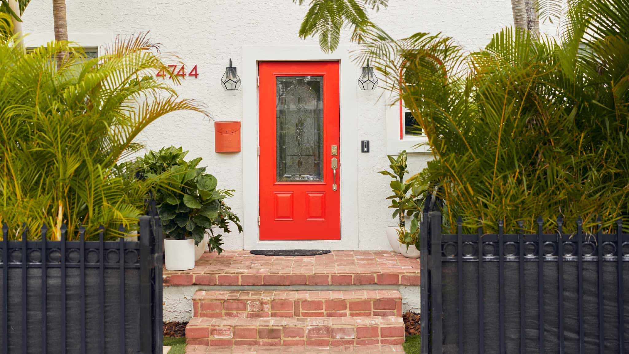 Bright red front door contrasting with light colored home exterior and black front yard fence