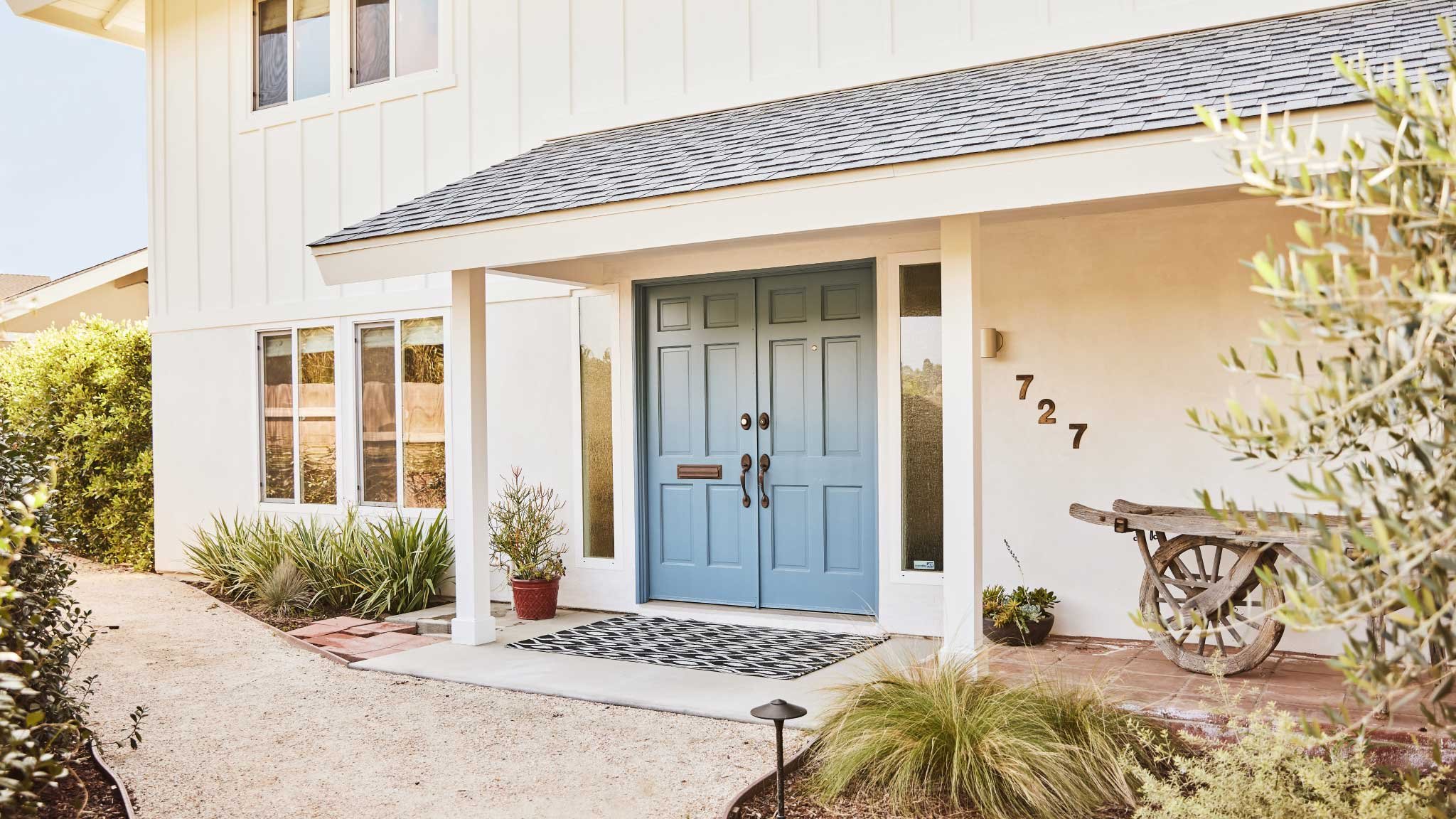 Stylish home facade with blue front doors, gravel path, and ornamental plantings in yard