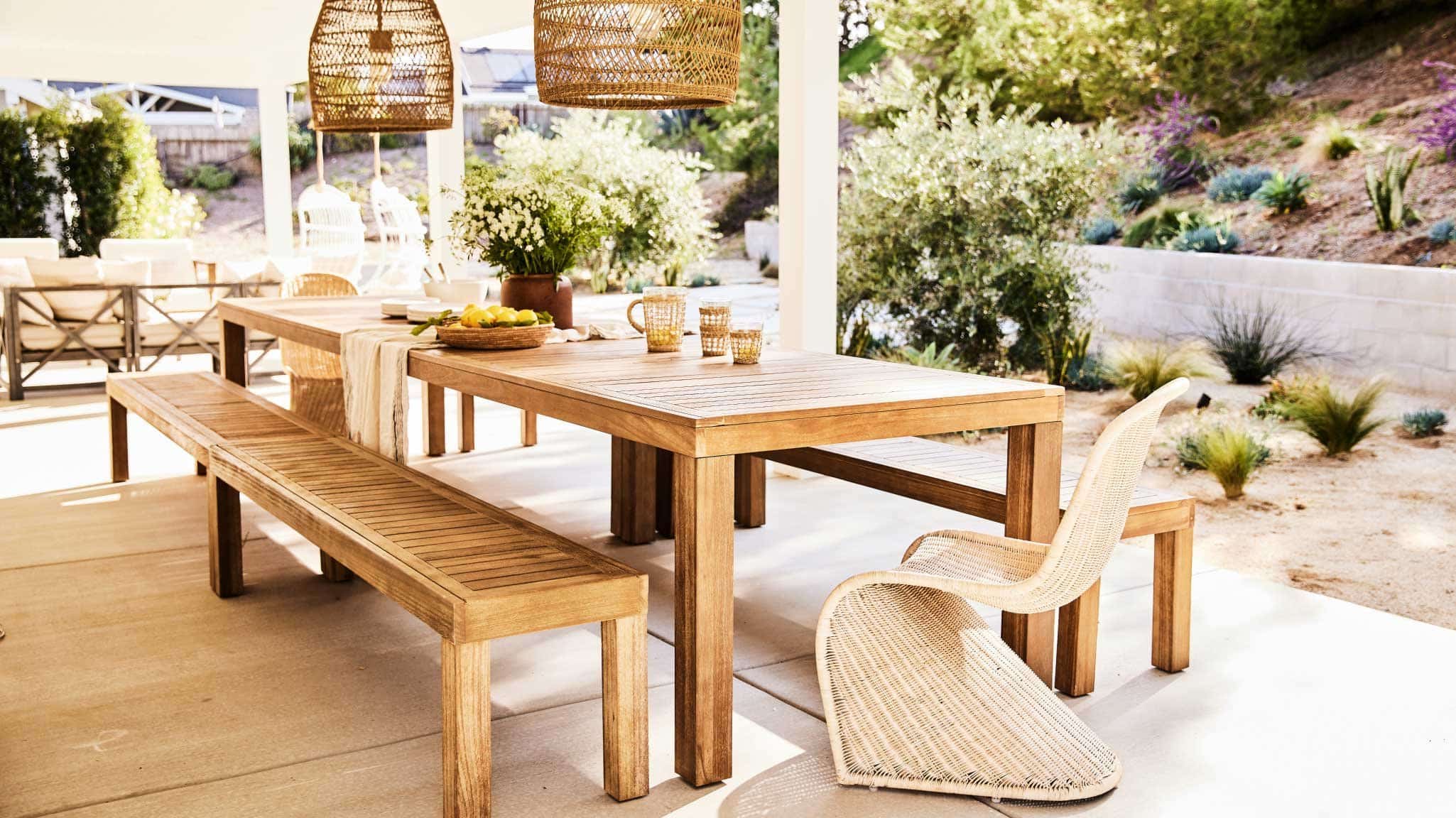 outdoor dining area on a backyard deck with drought tolerant landscaping and slope with retaining wall in background