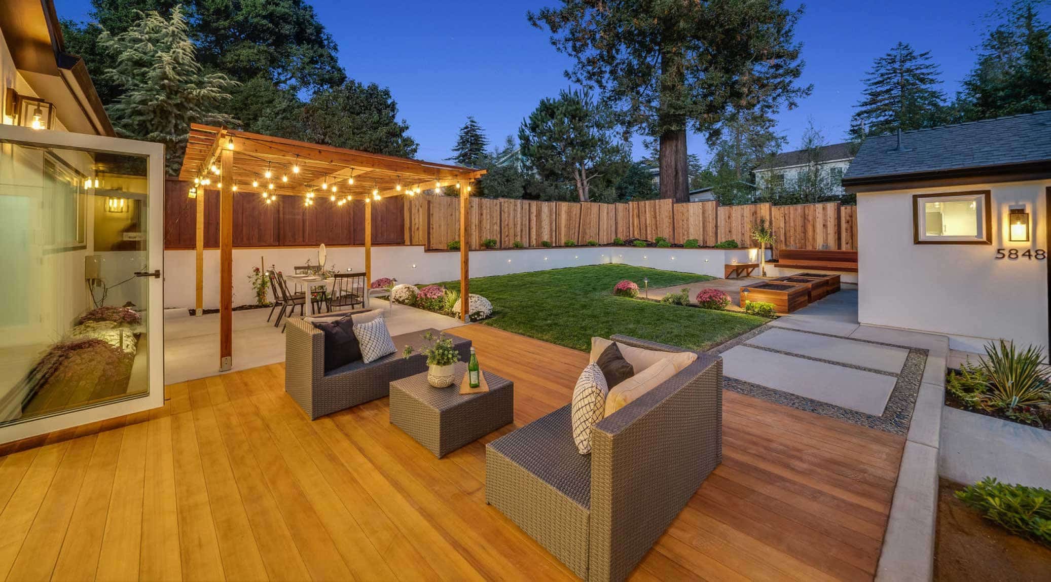 Finished backyard with lounge area on deck, pergola-covered dining area, and happy plants