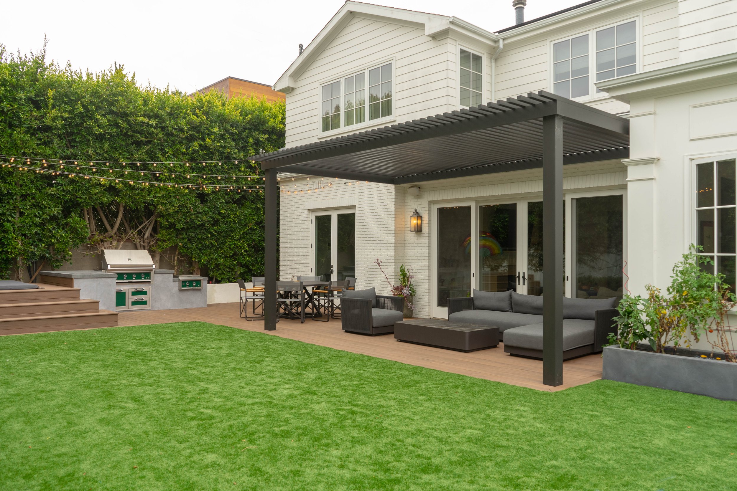 Backyard patio, outdoor kitchen, sitting and dining areas, pergola with whimsical light and a lawn