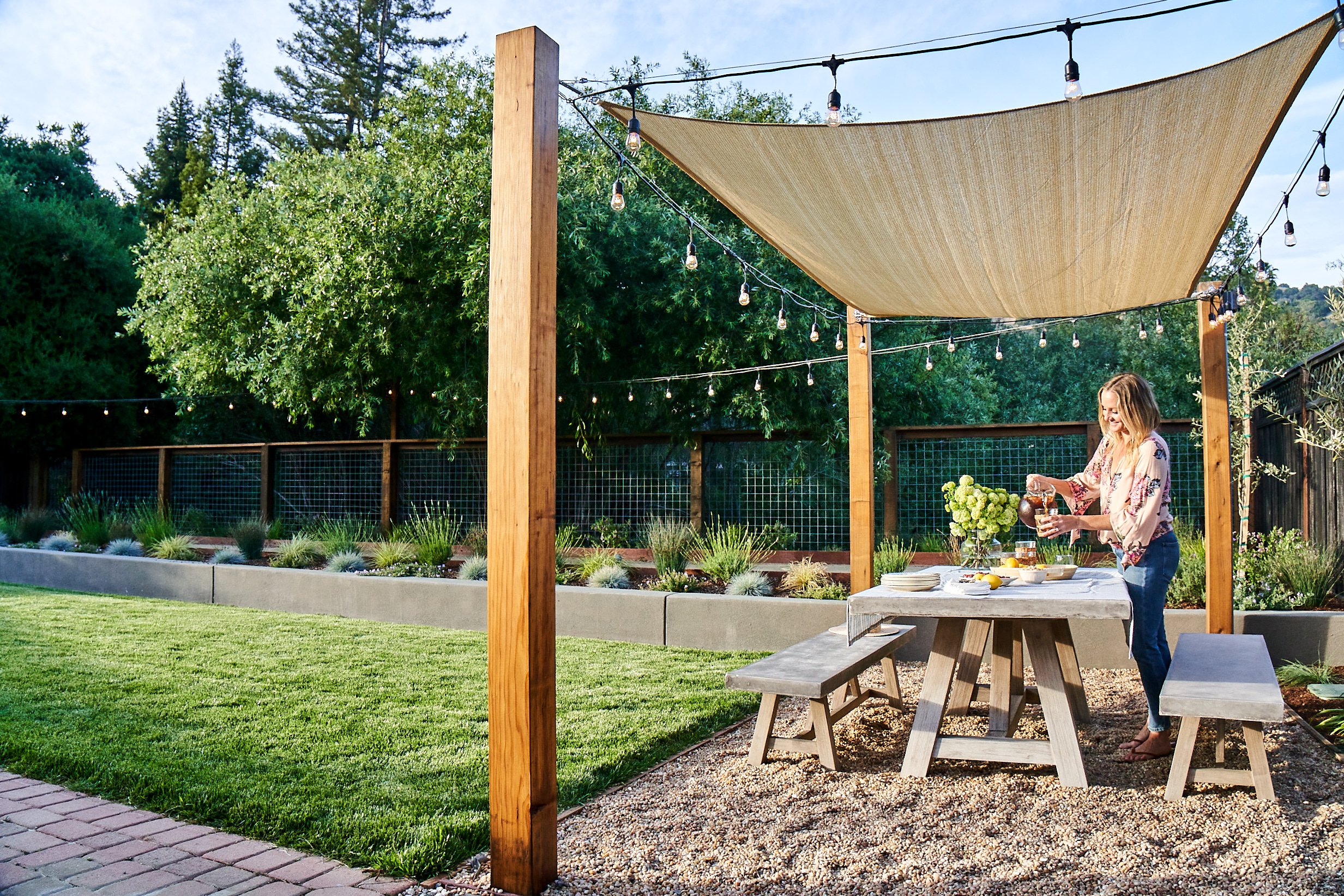 gravel dining area with four posts supporting a shade sail above