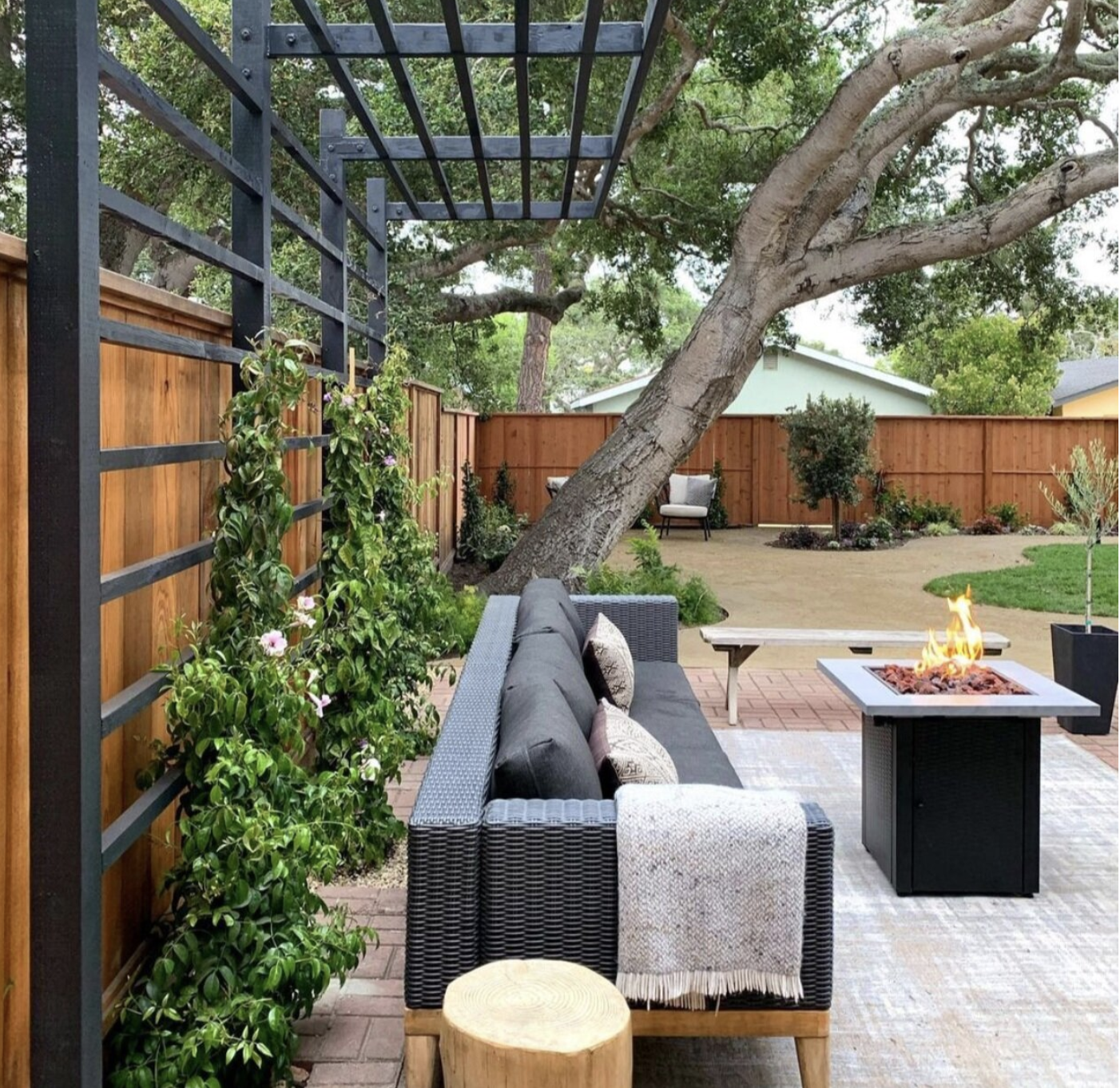 Fenced yard with a sitting area around a fire pit, trellis, and plants
