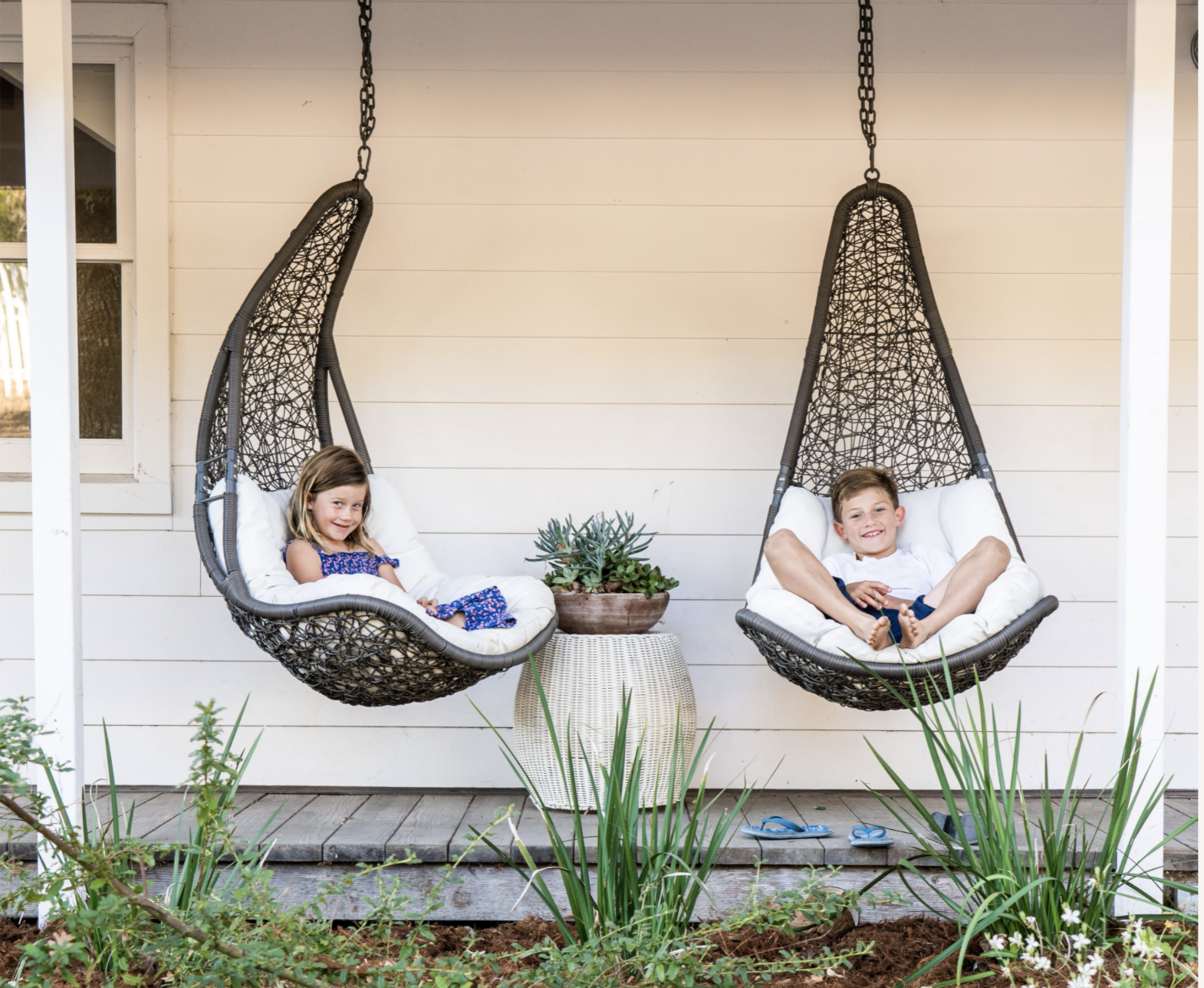 Two children seated in hanging chairs on porch