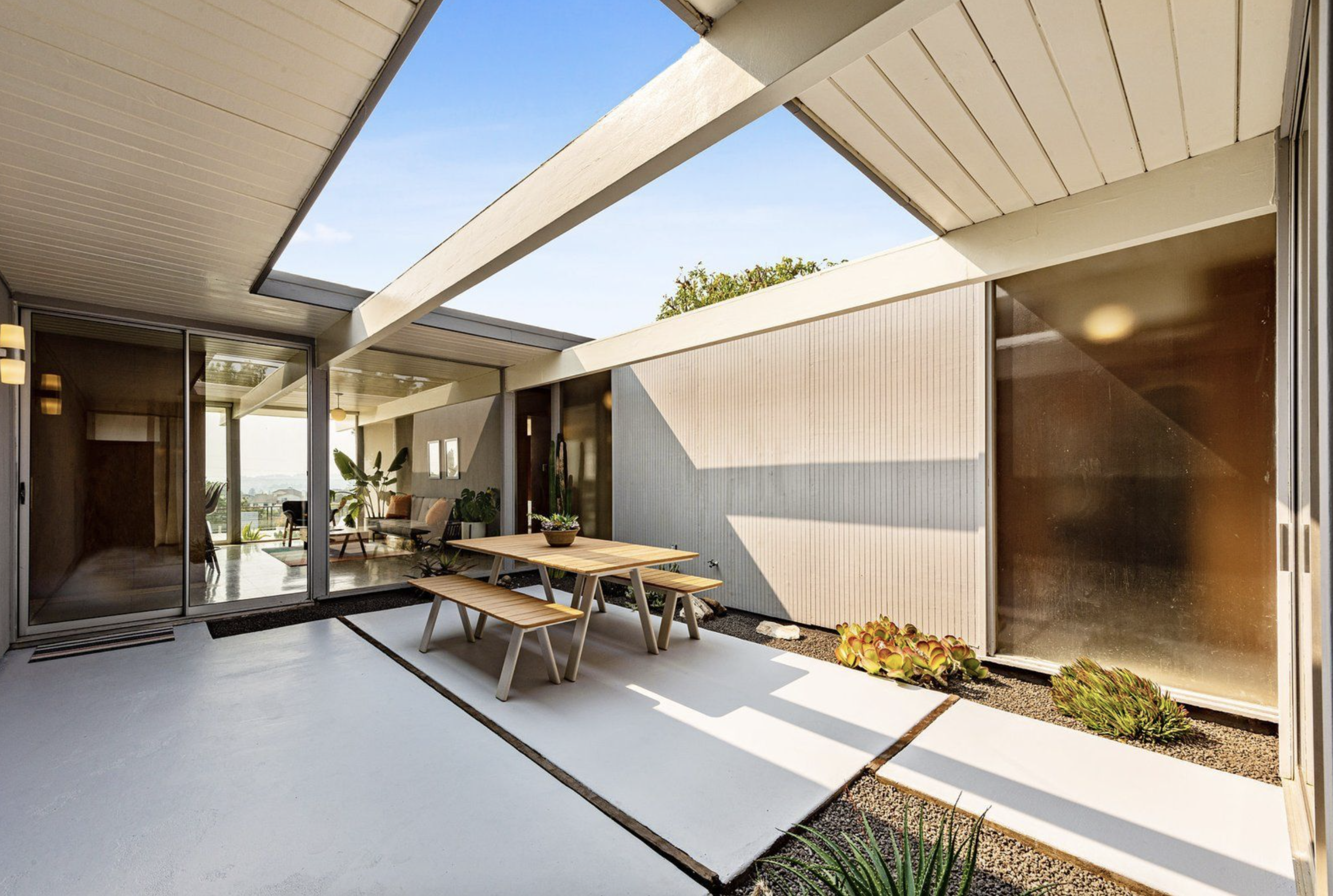 Open roof Eichler with concrete floors, outdoor dining set and ornamental plants