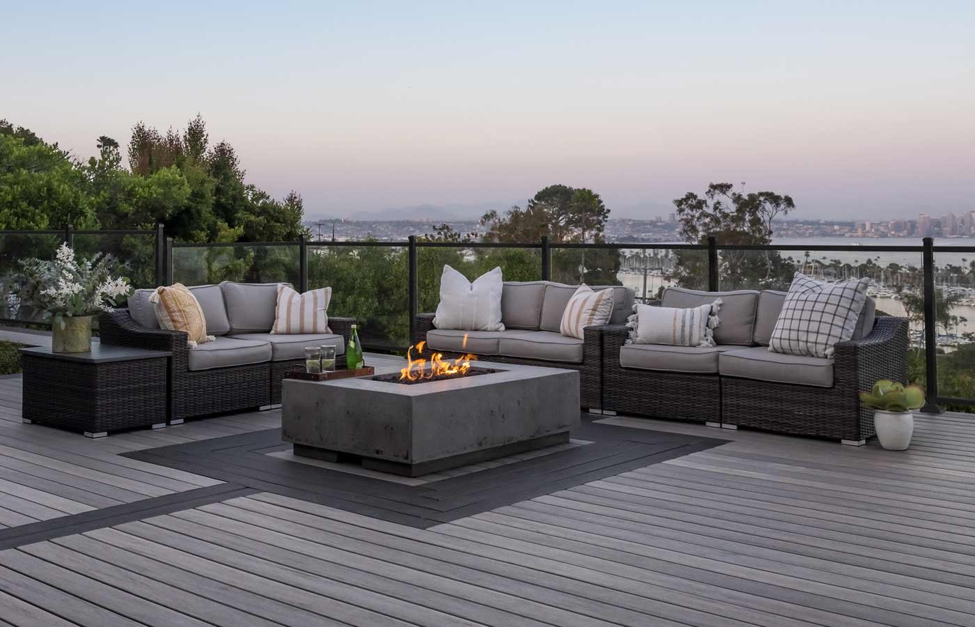A patio with a deck, sectional chairs and a fire pit