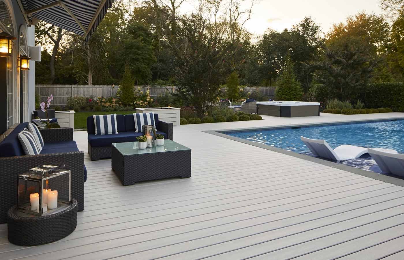 A pool with a deck, a sitting area, a hot tub and some plants around the yard