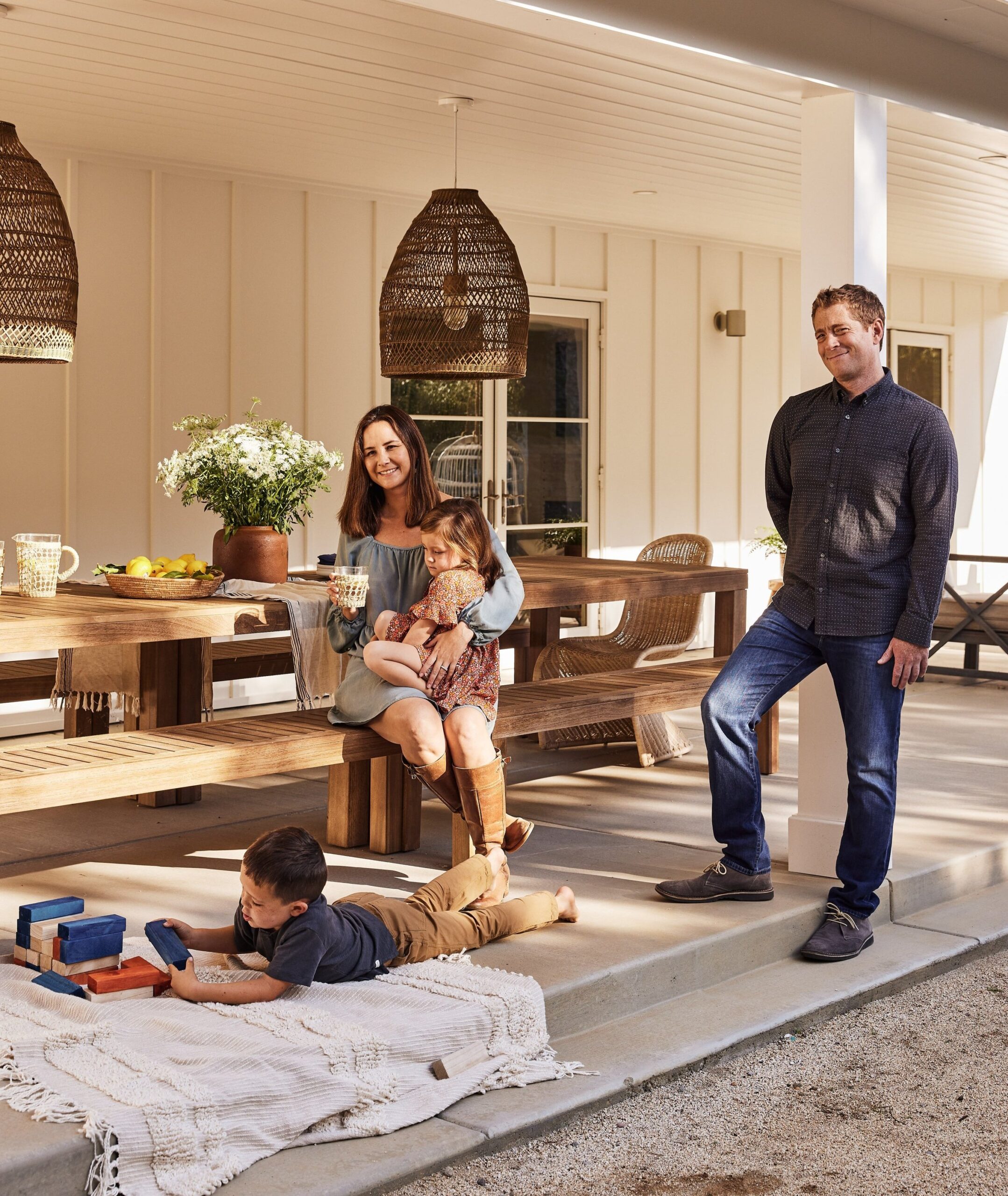 A family of four in a front yard with outdoor dining furniture and outdoor hanging lights