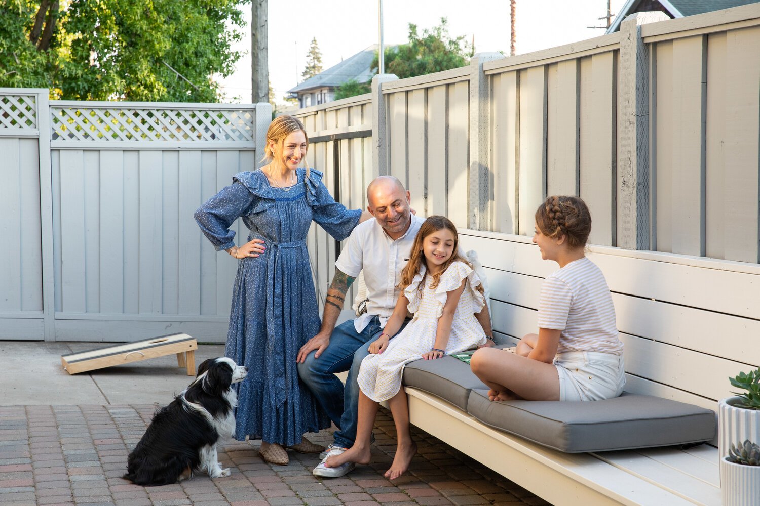 A family of four and their dog sitting in an outdoor sitting area in a fenced yard