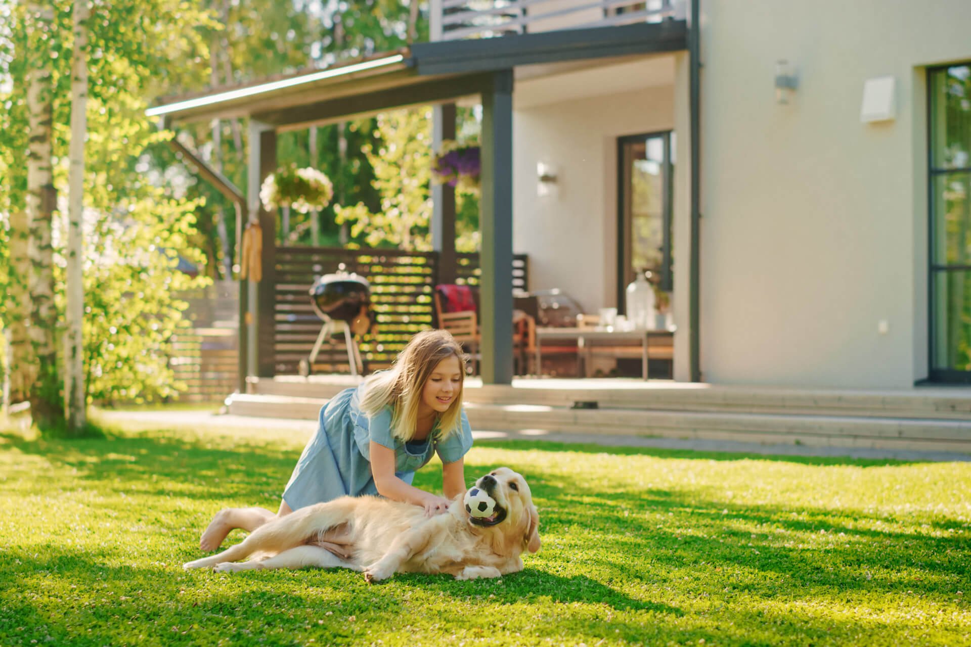 A girl playing with a dog on a lawn with a patio behind and a sitting area