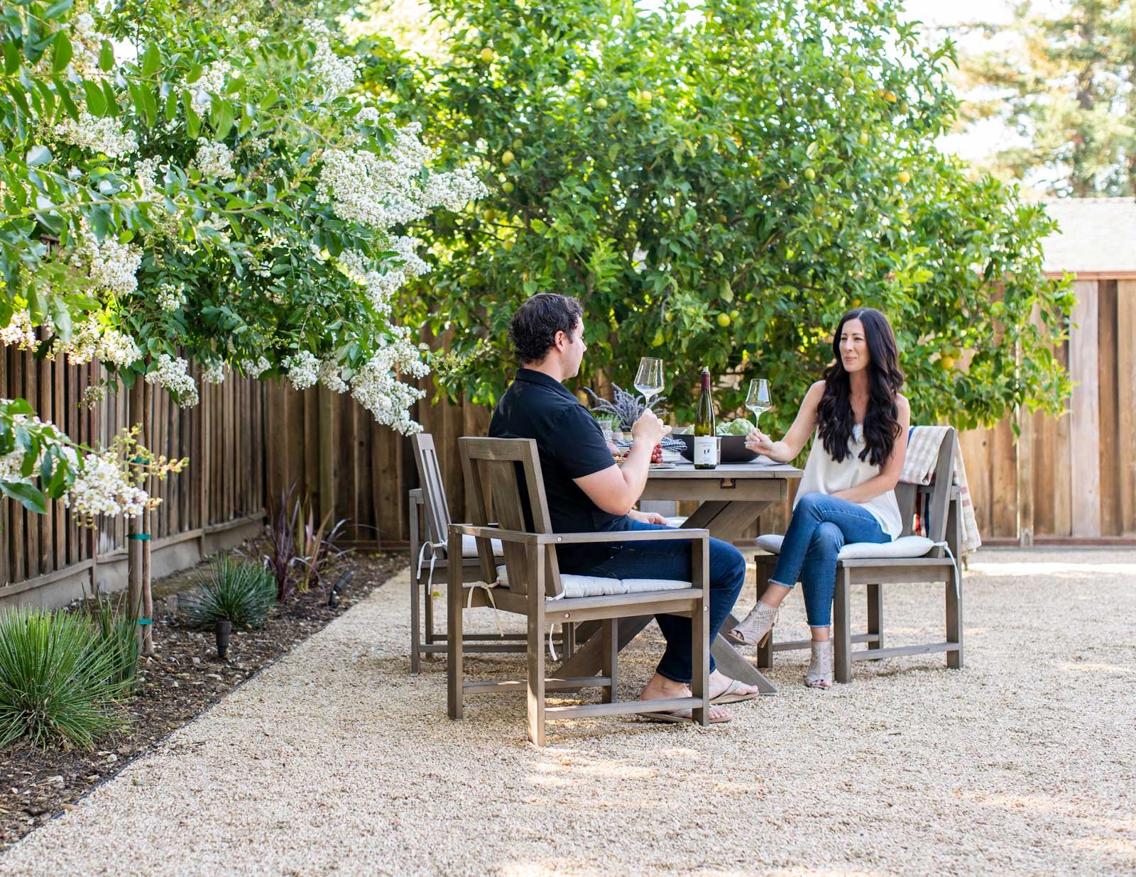 Fenced backyard with a man and woman sitting in a dining area with colored gravel.