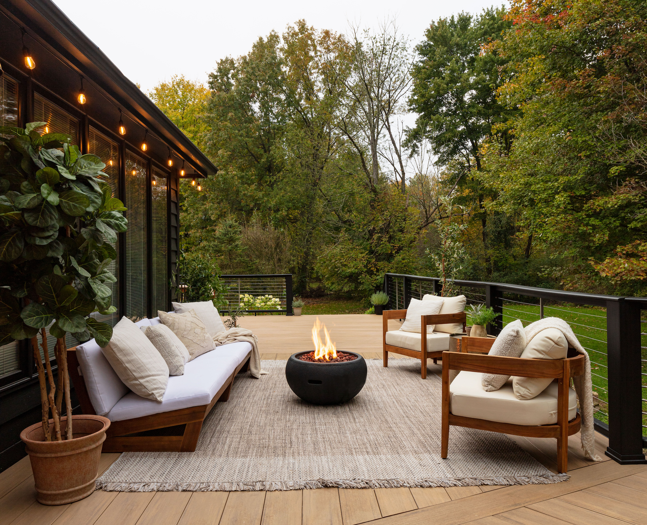 A backyard with TimberTech composite decking, fire pit with lounge couches next to tall trees