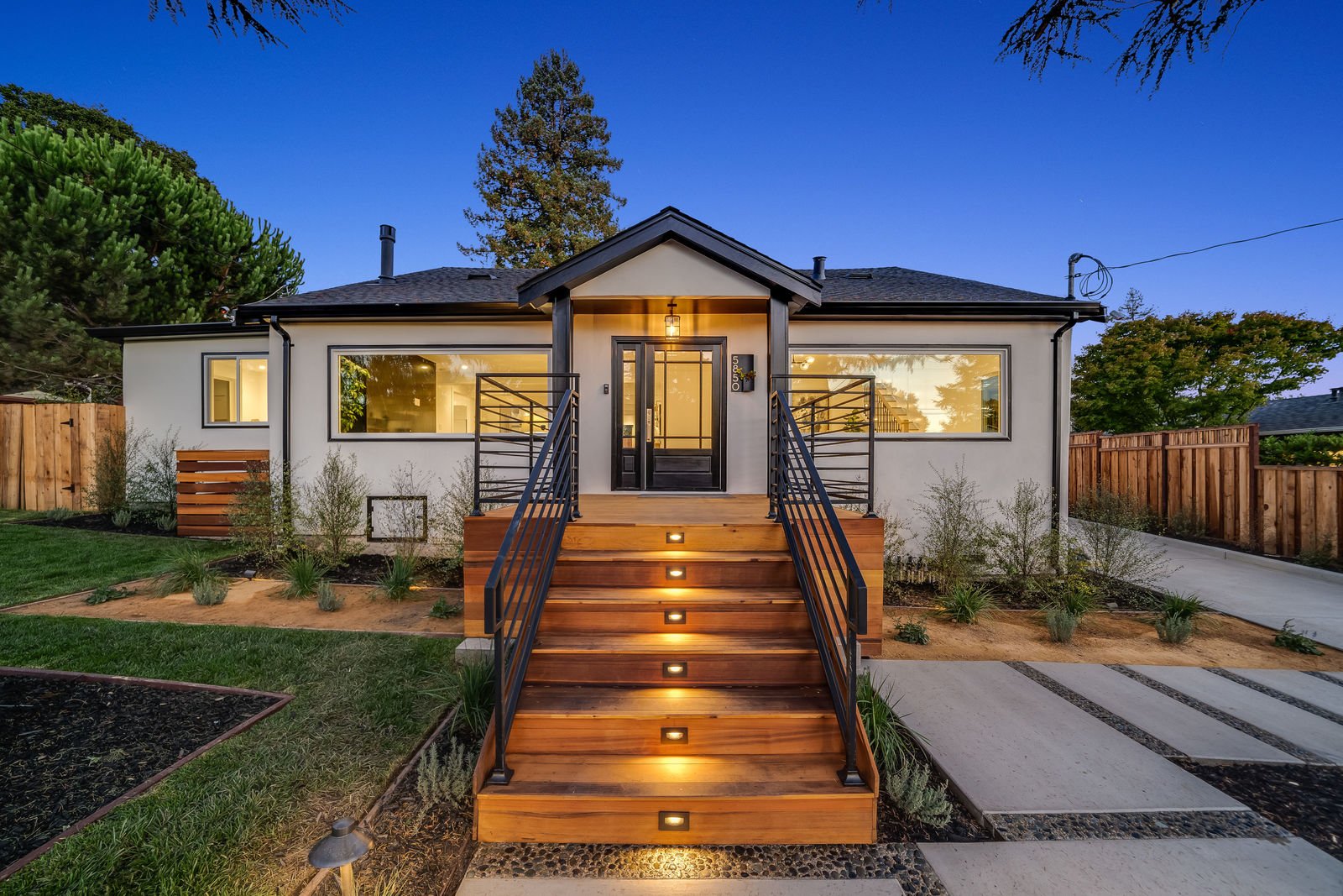 Front of modern home with small wooden porch, modern black railing, deck lighting on porch steps and a hanging light above the outdoor entryway