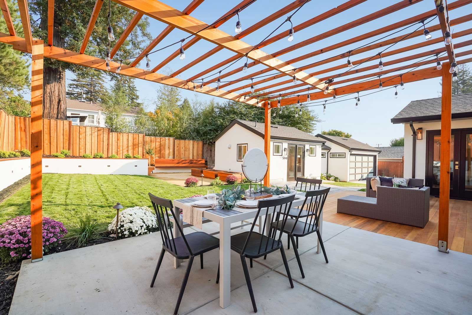 A wooden fenced yard with a patio, outdoor dining, rattan garden sofa and decorative plants.