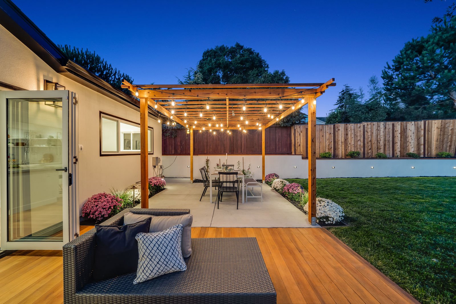 Side view of a back deck and concrete patio with overhead wooden pergola covered in string lights