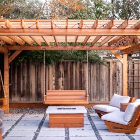 Wooden pergola over paver patio and matching fire pit with hanging benches and lounge chairs