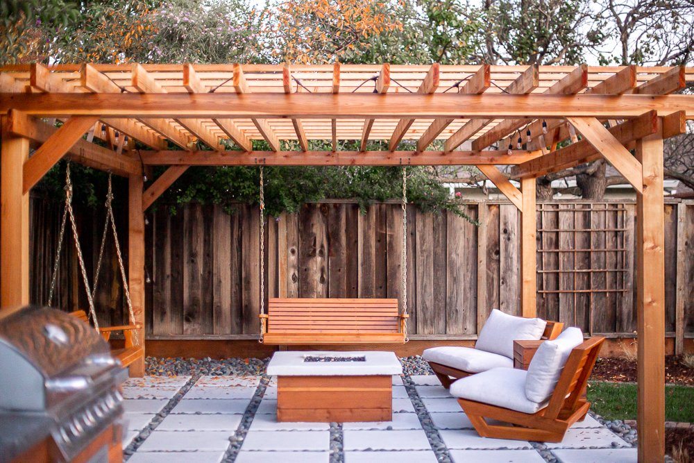 Modern cedar pergola with swinging benches above a concrete paver and gravel patio with fire pit