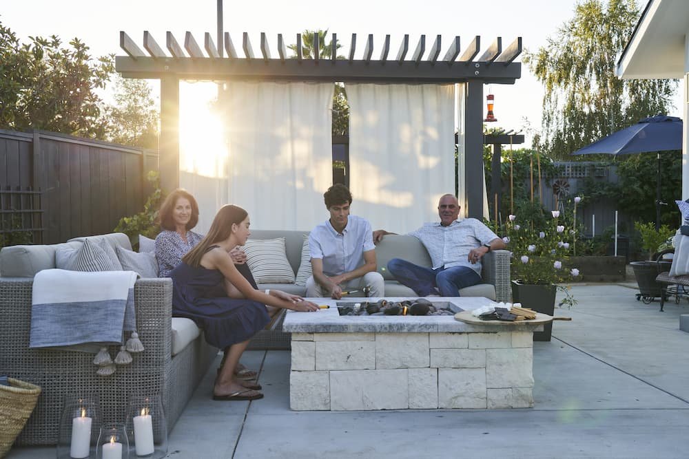 family sitting around outdoor fire pit with cantilever pergola and shade curtain blocking direct sun behind them