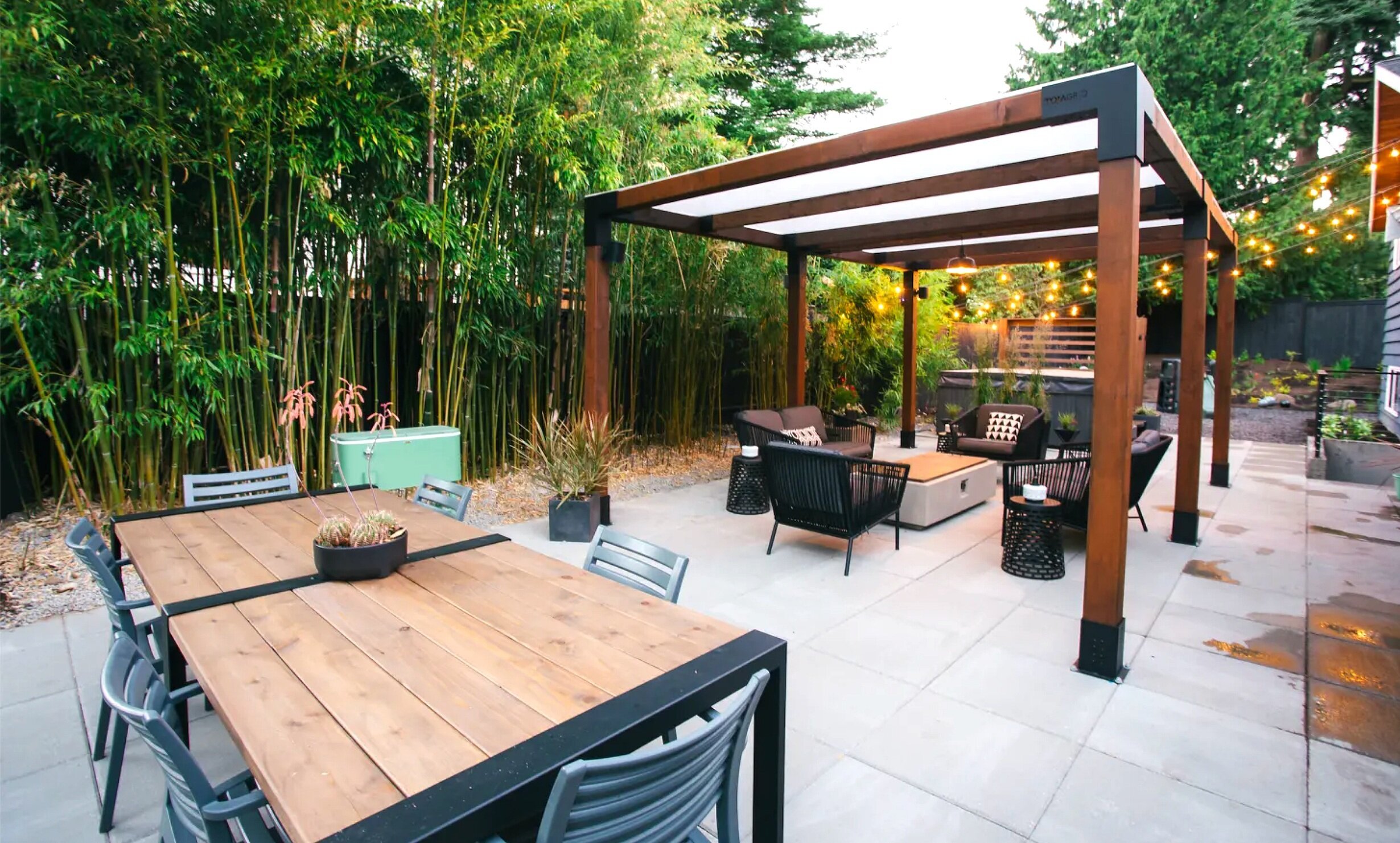 a paved backyard with fence and bamboo for privacy and pergola with clear roof shading a fire peat seating area