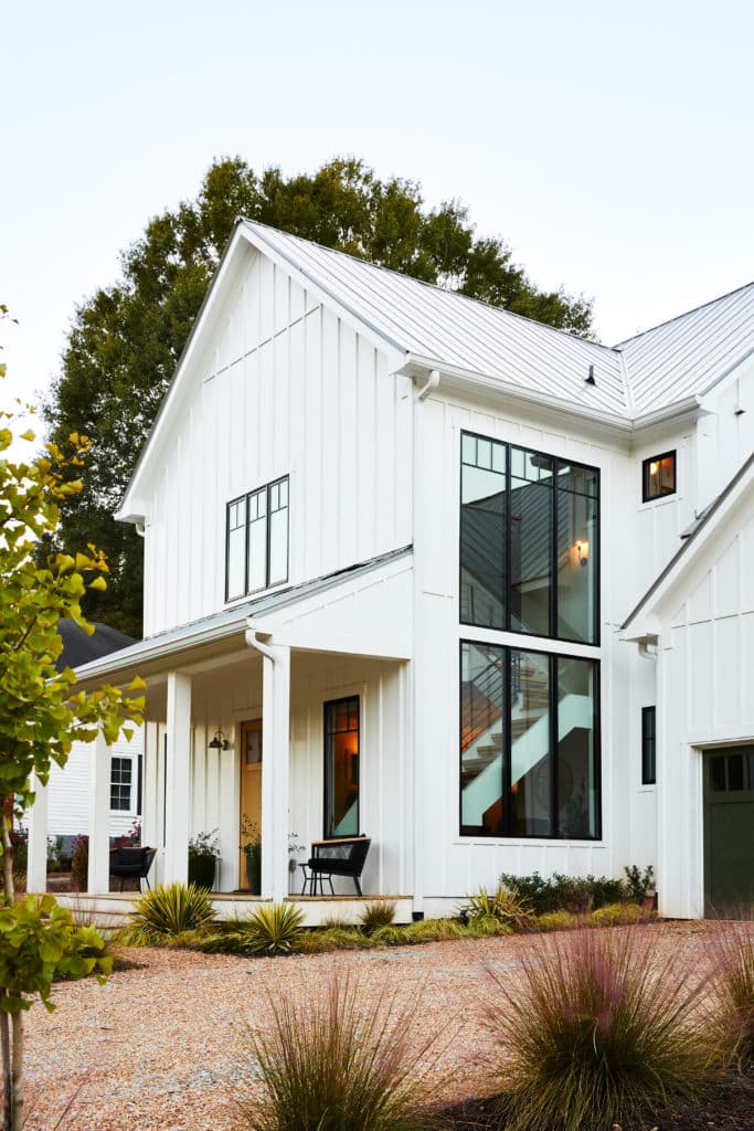 Side view over gravel driveway of modern farmhouse style home with large windows.
