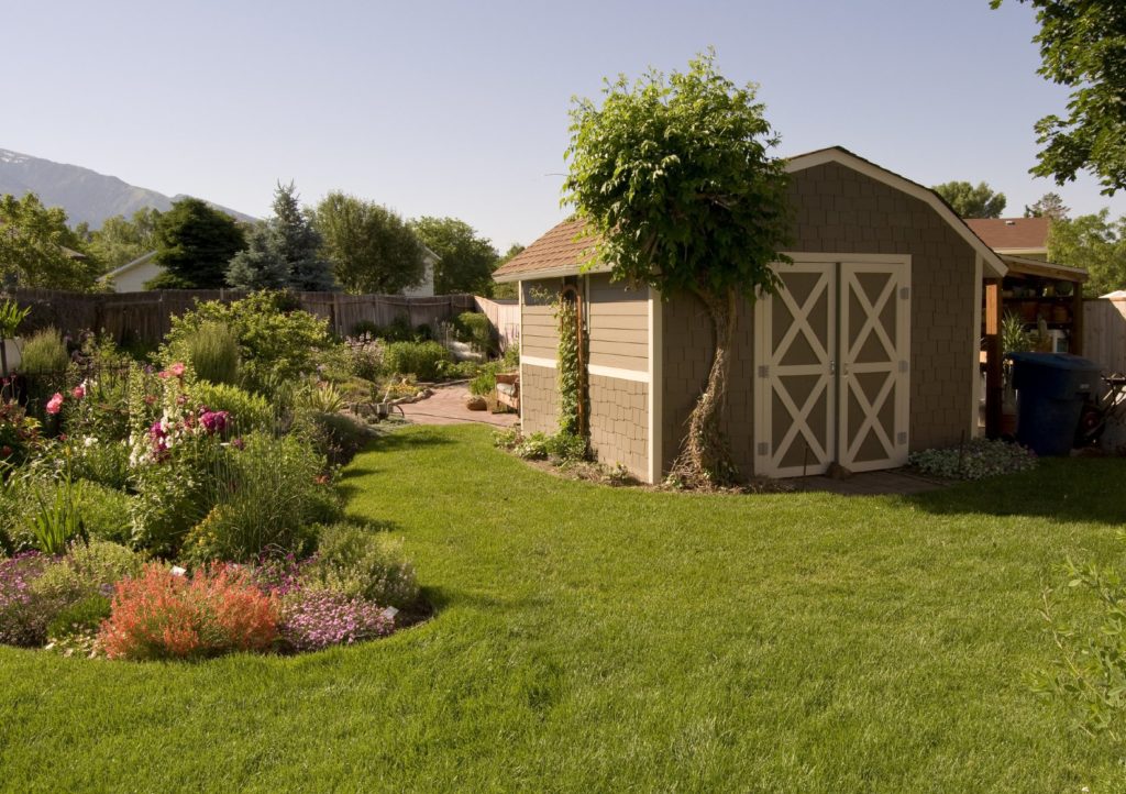 Large traditional shed with plantings surrounding it, usable lawn, and adjoining patio