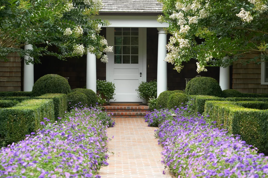 Traditional style front porch and brick walkway with evergreen hedges and purple flowering groundcover on either side