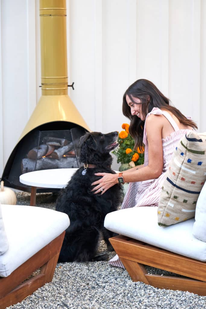 Kristy with her dog sitting on an outdoor lounge chair next to their midcentury modern outdoor fire place
