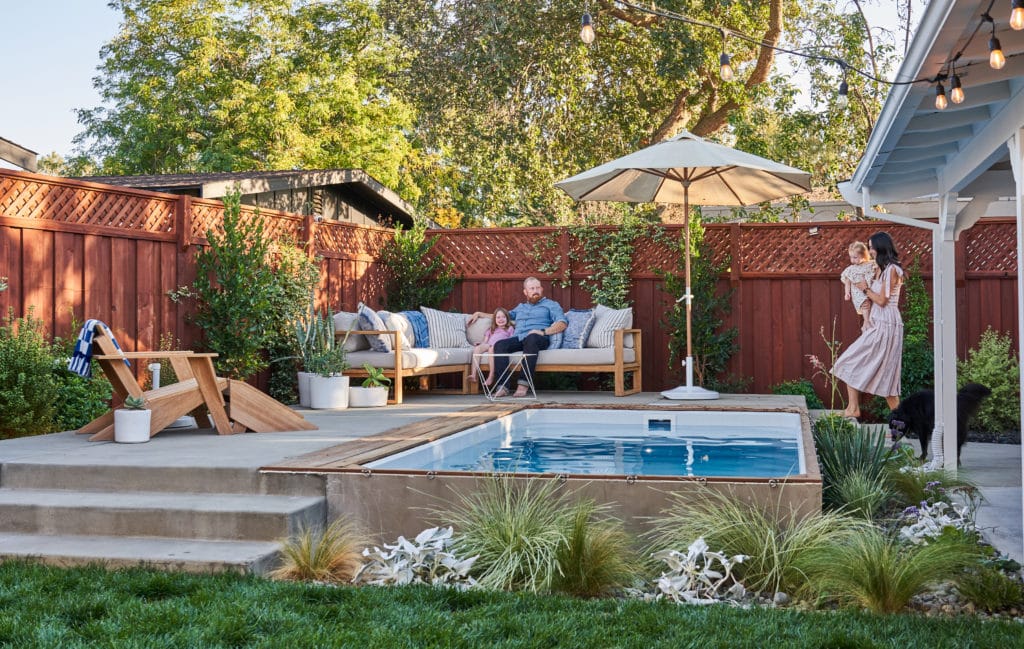 Man, woman, and two young children on a raised concrete patio with outdoor sectional and adjoining raised plunge pool.