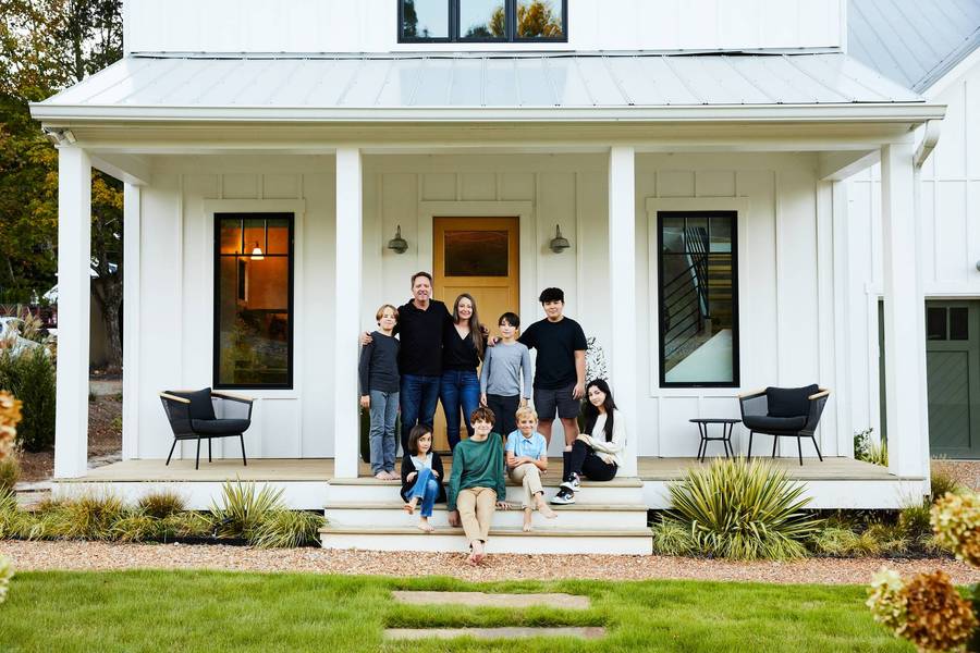 Man, woman, and seven children on a front porch of a modern farmhouse style home. 