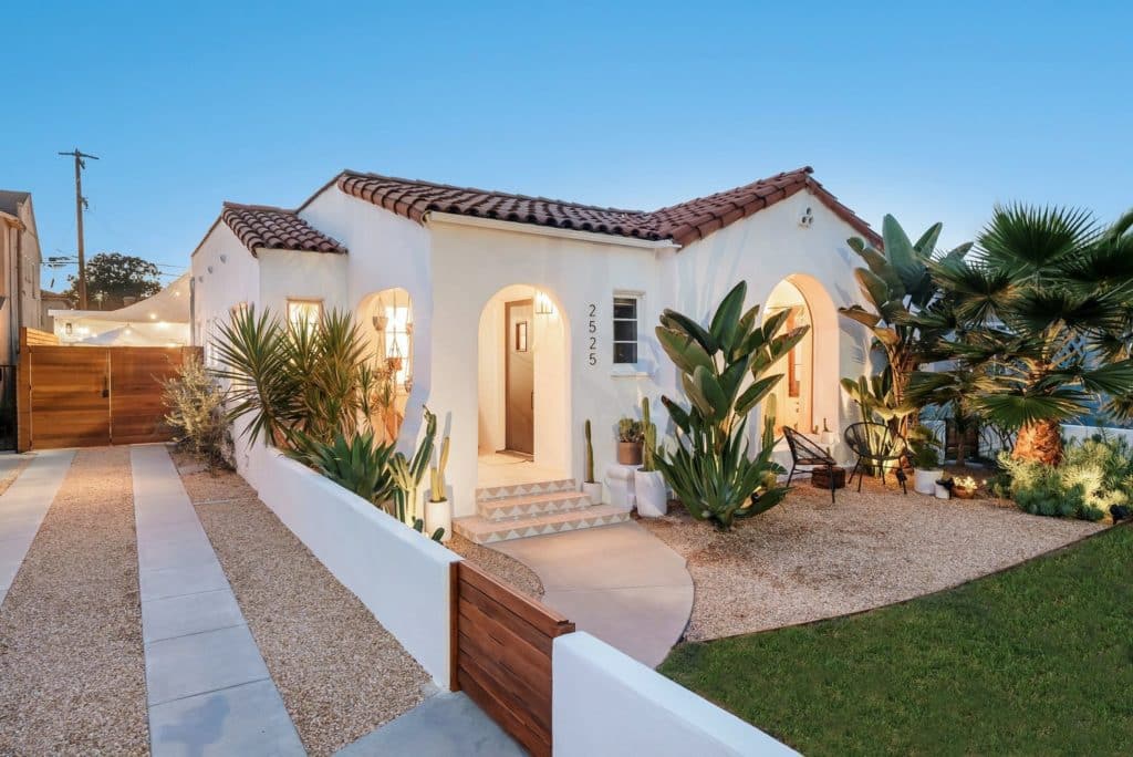 Front of southwestern style home with modern outdoor wall lights and hanging plants on a covered porch and decorative tile on front porch step risers