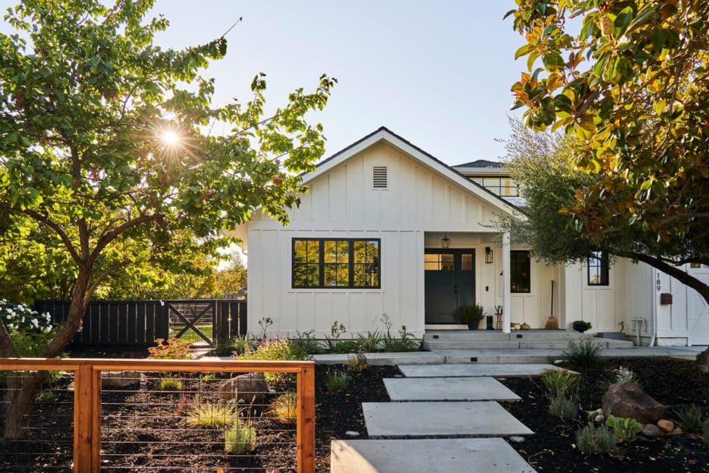 Modern farmhouse style home with concrete patio, large concrete paver path, dark-colored mulched front yard with drought tolerant plants, and modern wooden and wire front yard fence