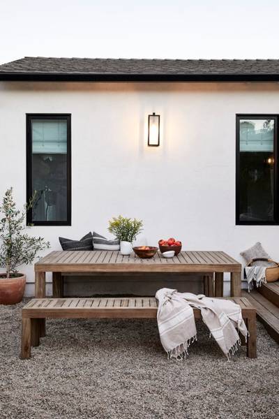 Outdoor dining table and benches on gravel in front of white home exterior