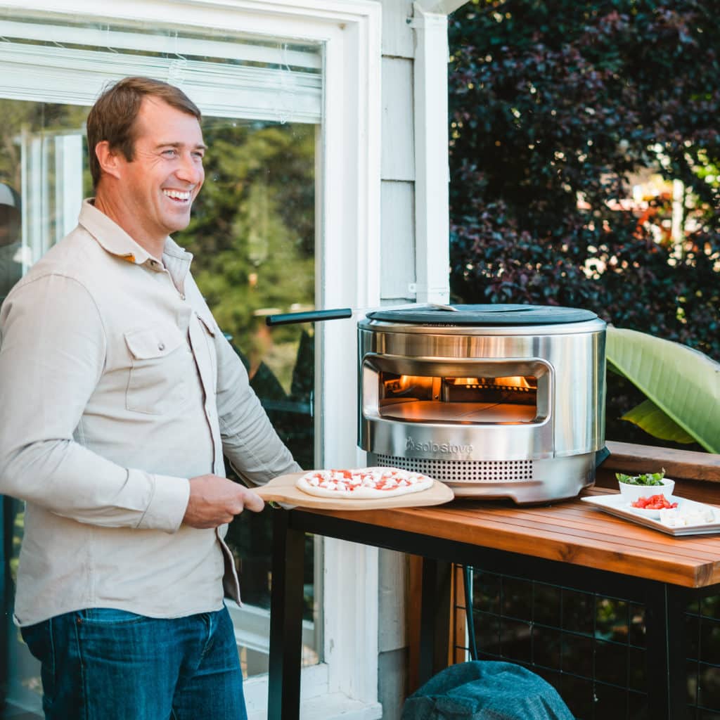 Man holding uncooked pizza near pizza oven