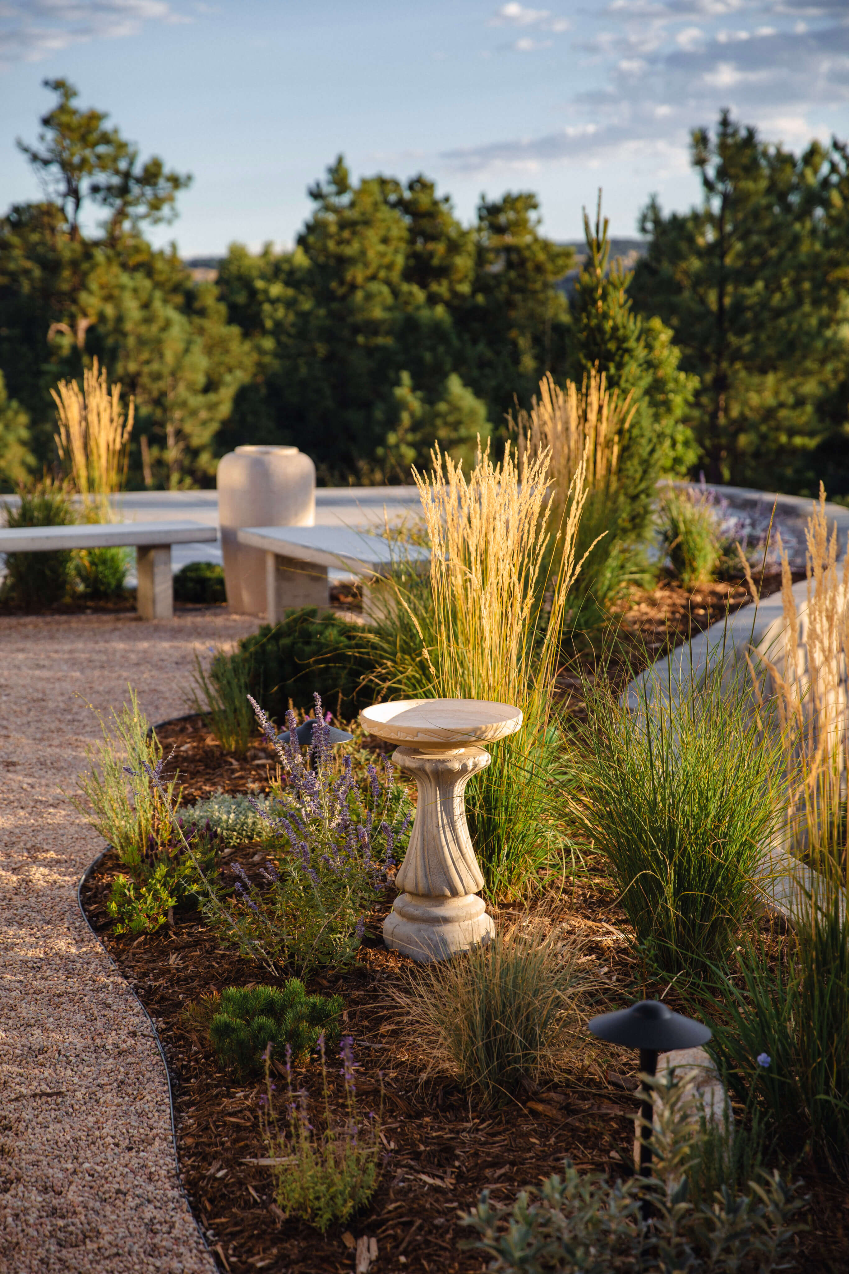 A small water feature in a planting bed, surrounded by ornamental grasses and other plants.