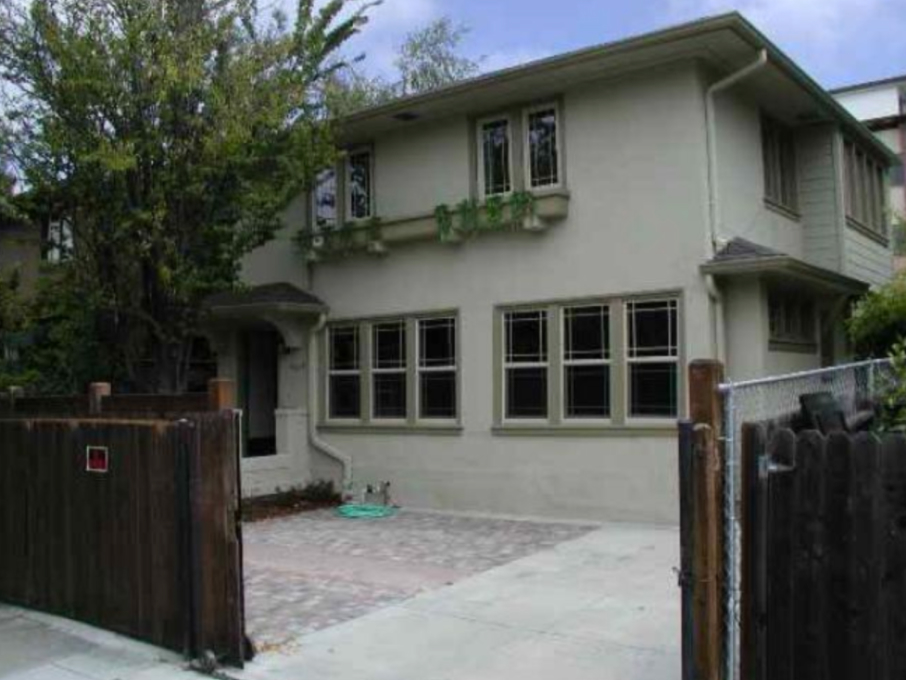 Drab front yard and two story home with olive exterior and brown front gate across property