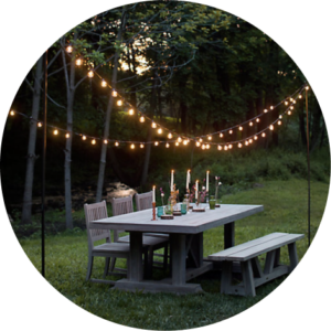 Dining table in yard with candles on top and string lights overhead.