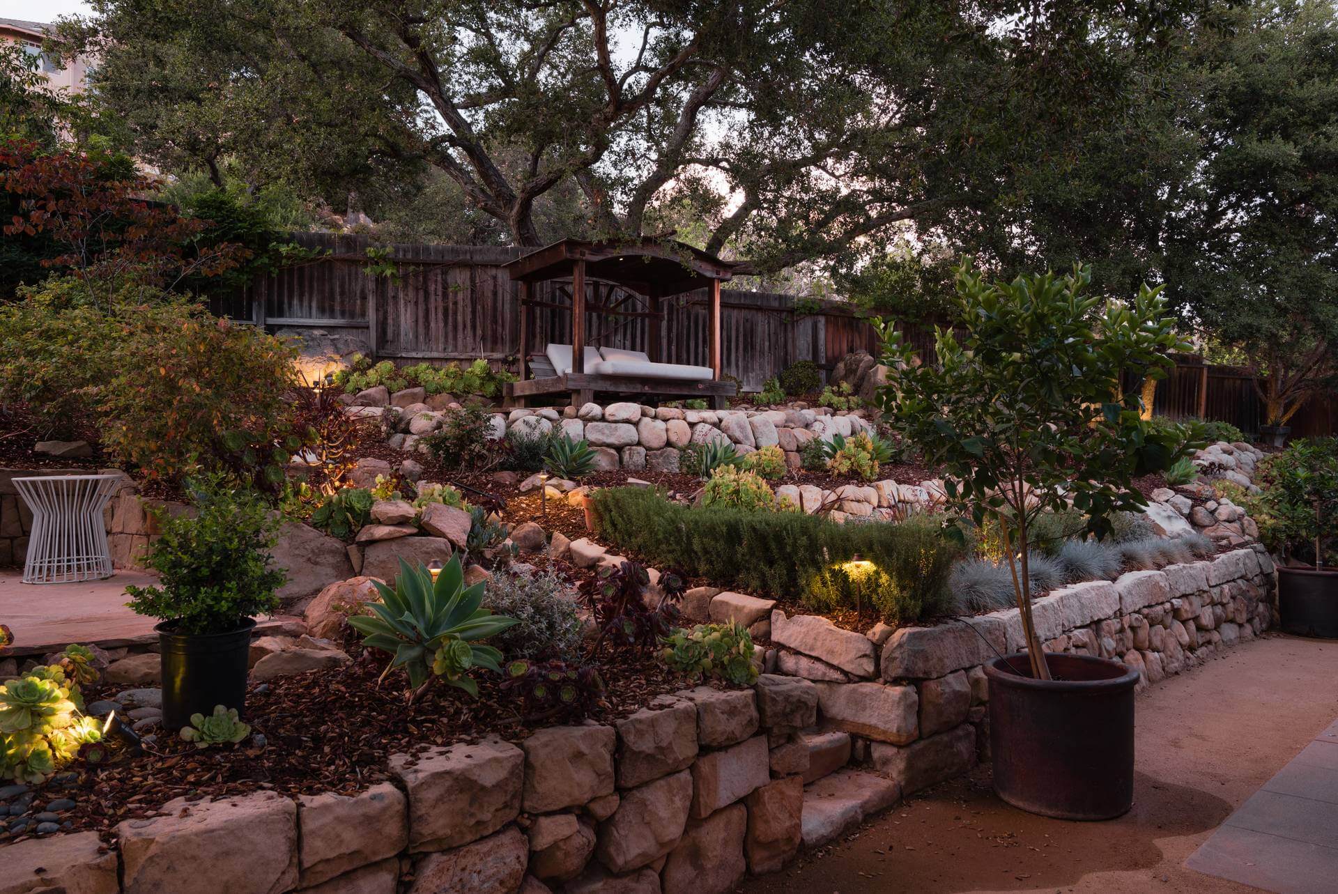 Stone wall with lush planting in a sloped backyard designed by Yardzen