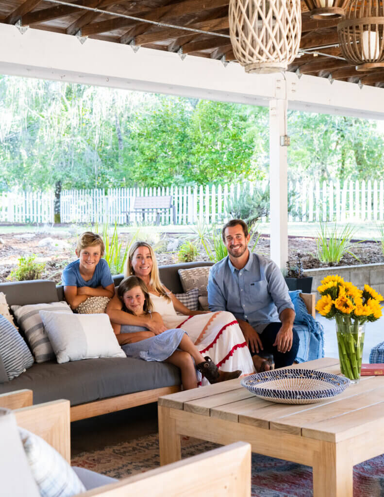 Family, including mother, father, son and daughter sitting on an outdoor couch beneath a reimagined car port