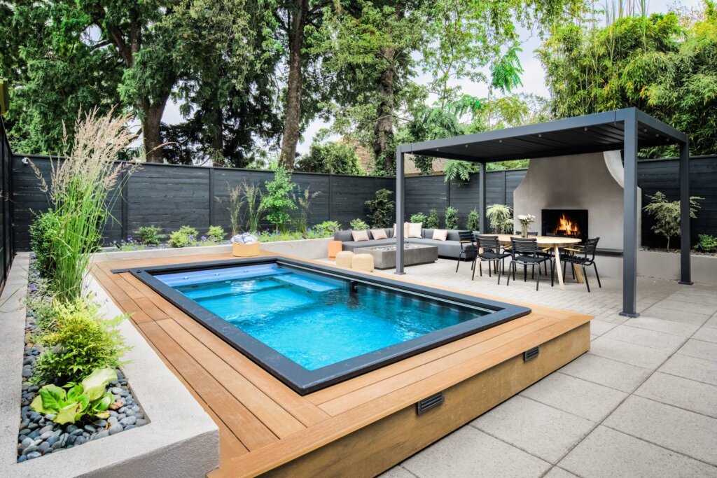 Plunge pool with small deck near black metal pergola covered outdoor lounge area with fireplace