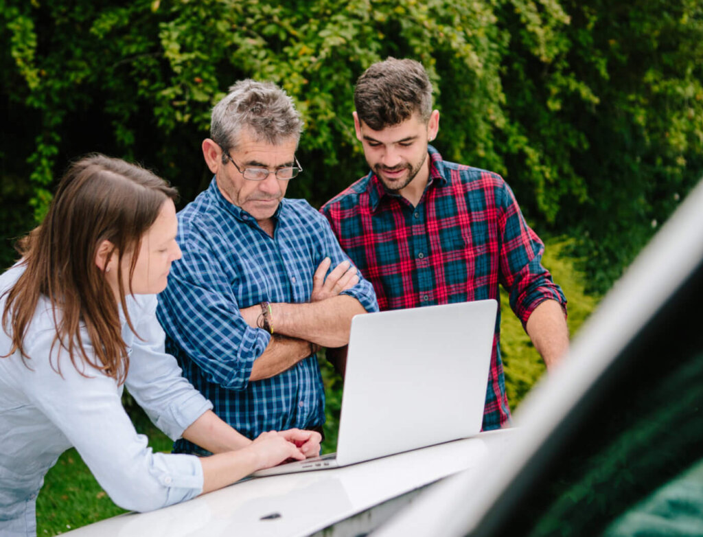 A landscape contractor showing clients a design on a laptop on the hood of a pickup truck