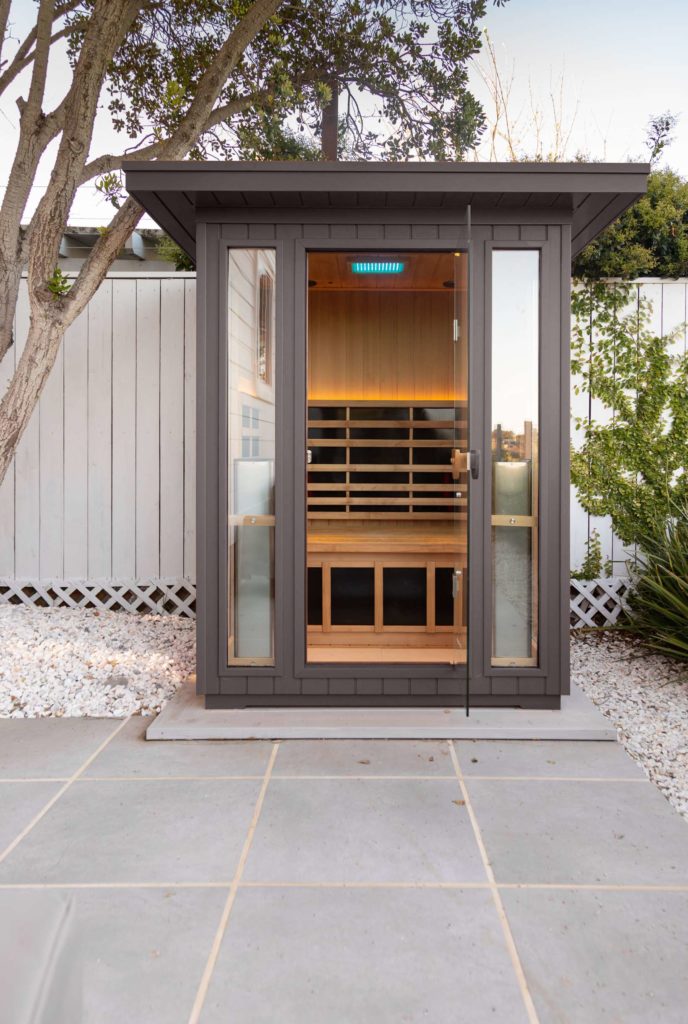 The Clearlight Sanctuary Outdoor 2 Sauna on the perimeter of a paver patio in a modern backyard