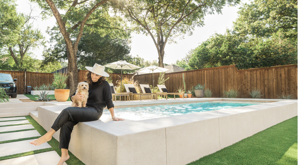 Woman holding small dog seated on the edge of a plunge pool in backyard