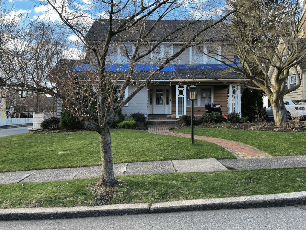A photo of the front of the historic home, before updates were made. A tree with no leaves in the winter and the roof with constructions materials on top.