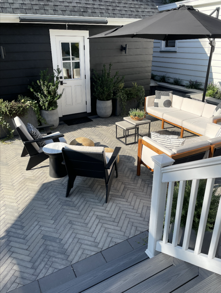 a photo of the client's backyard patio area from the viewpoint of the back steps. A lounge area is backed by potted plants along the garage wall.